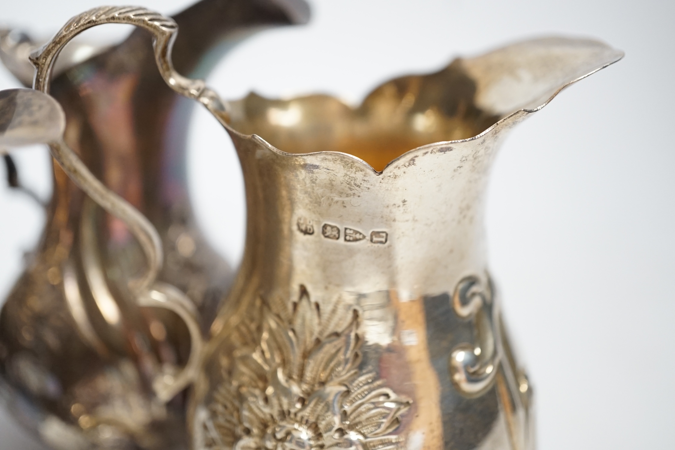 A George III inverts pear shaped cream jug with later embossed decoration, 11.2cm and three later silver cream jugs including two Victorian, 17.4oz.